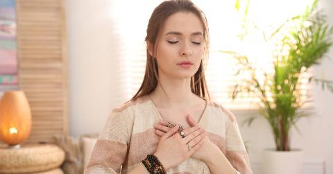 A woman with her eyes closed, her hands over her heart, looking peaceful.