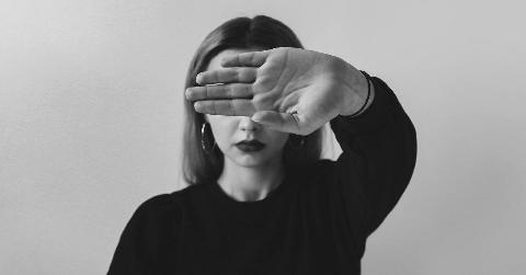 A greyscale image of a woman holding her hand out in front of her, palm out, blocking her eyes.