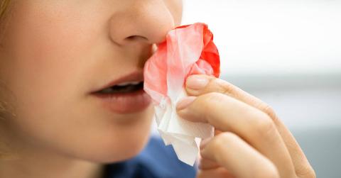 Someone holding a bloodied tissue to their nose.