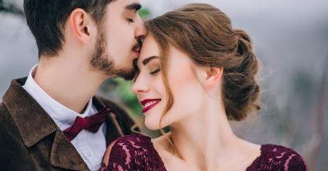 A couple close together, the man kissing the woman's forehead.