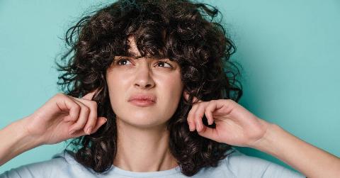 A woman with an annoyed expression plugging her ears.