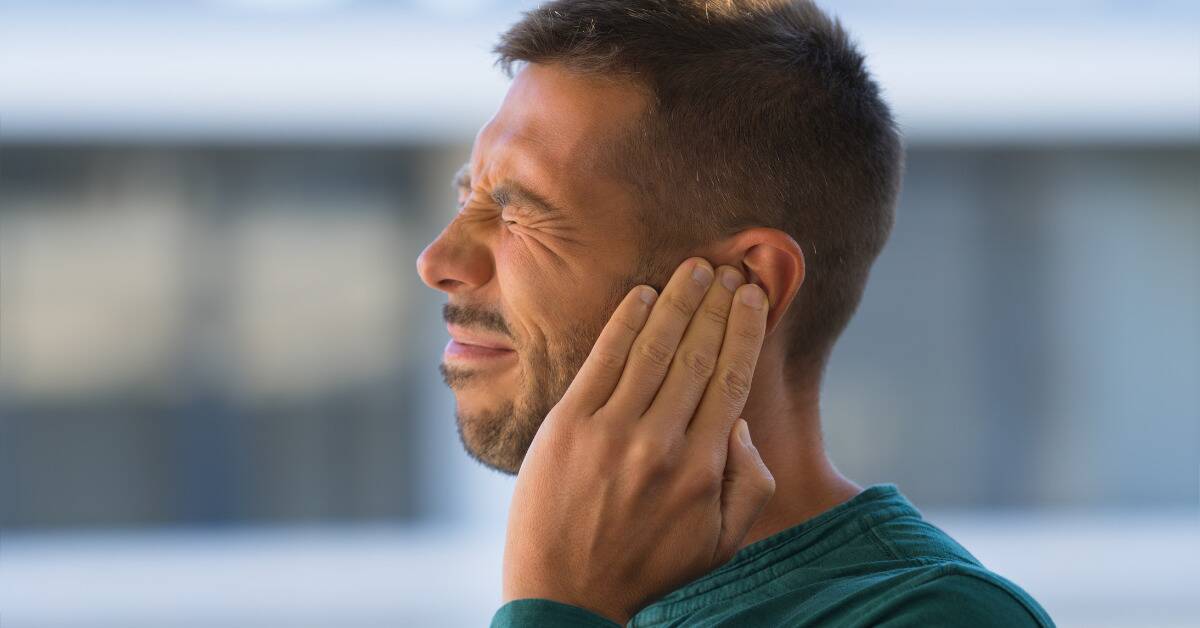 A man covering his ear with his eyes shut tight.