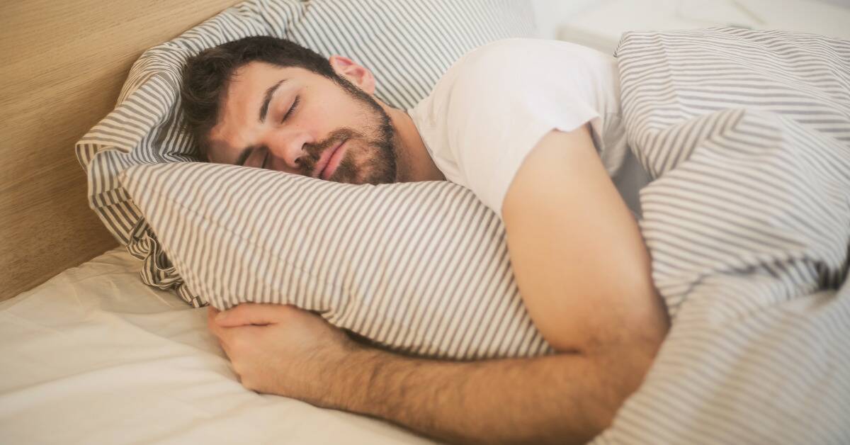 A man asleep in bed, hugging his pillow.