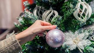 A close shot of a woman putting a silver ornament on a Christmas tree.