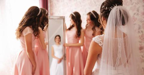 A bride seeing herself in her dress in the mirror, surrounded by her bridesmaids.