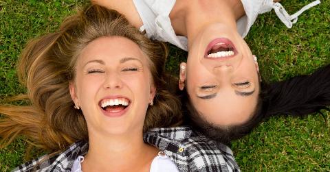 Two friends laying in the grass, their heads side by side but facing different directions.