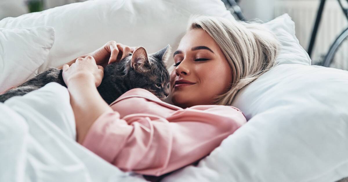 A woman laying in bed with her cat being held against her chest.