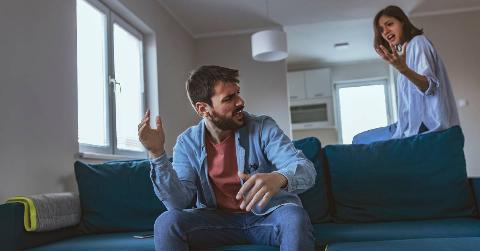 A man on the couch being yelled at by his girlfriend, yelling back at her.