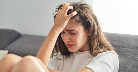 A woman with a hand to her head, eyes closed, looking stressed and upset.