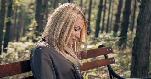 A woman sitting alone on a bench outside, looking down.