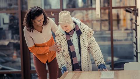 A woman helping an elderly woman stand up from her seat.