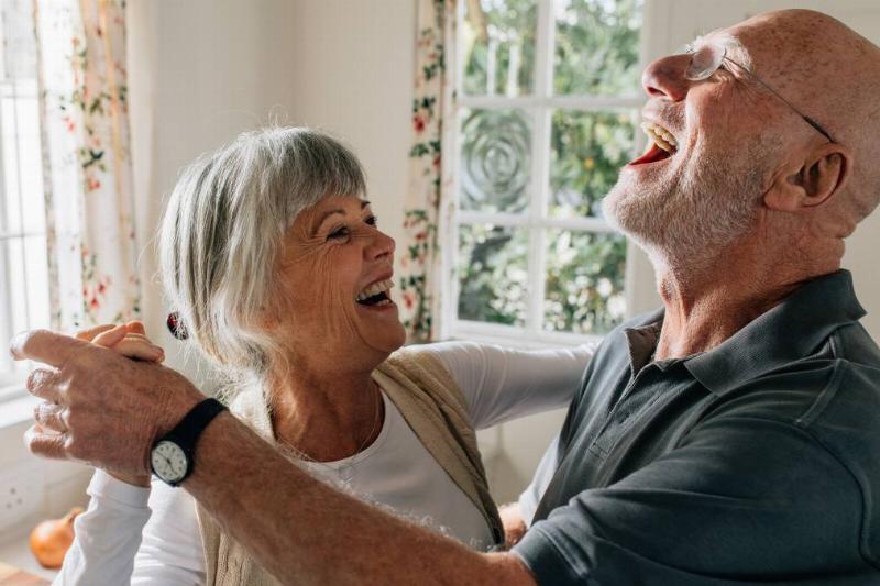 An older couple dancing in their home, both smiling and laughing.