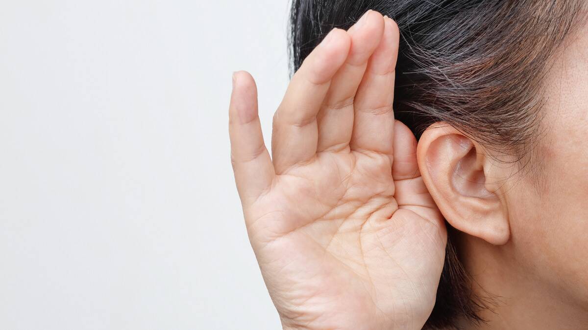 A close shot of a woman cupping her hand around her ear, signifying she's listening.