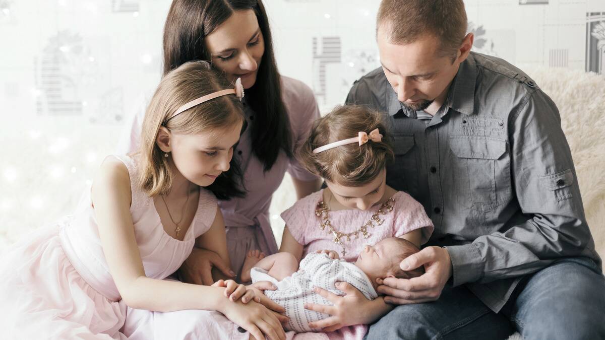 A family all gathered together, both parents and two young daughters, the youngest daughter holding a baby, the latest addition to their family.