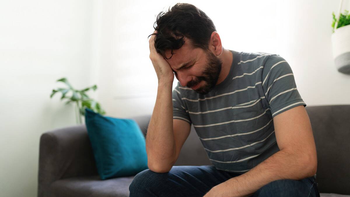 A man sitting on his couch, head in his hand, visibly upset/crying.