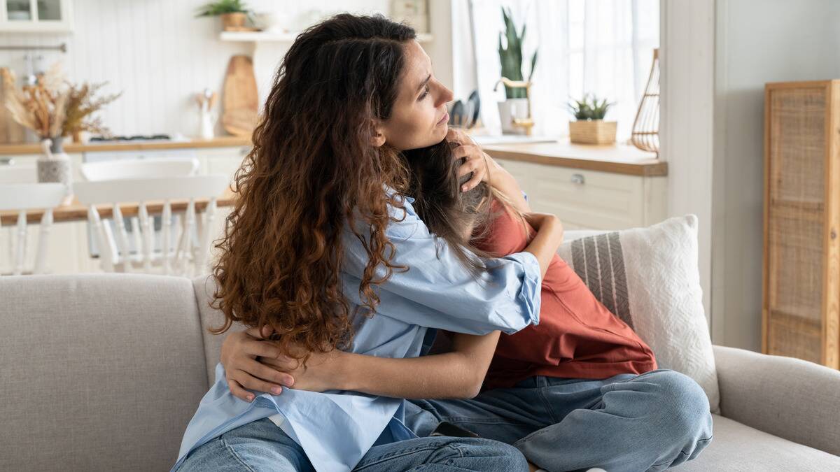 A mother hugging her daughter incredibly close as they sit on a couch together.