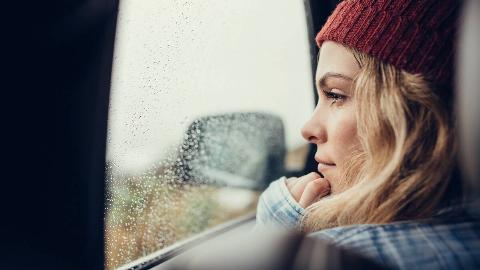 A close shot of a woman looking out a rain-covered car window.