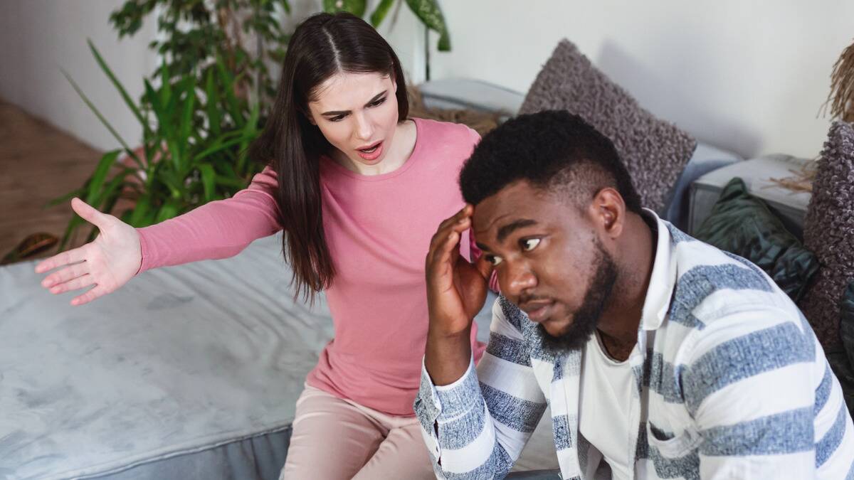 A man sitting on a couch with a woman sitting next to him, yelling at him as he tries to ignore her.