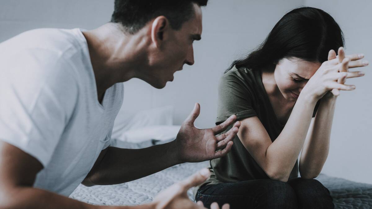 A woman looking stressed and sad, eyes closed shut, forehead in her hands, while a man sitting next to her yelling at her.