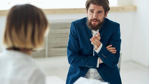 A man looking confused as he speaks to a woman sitting across from him.