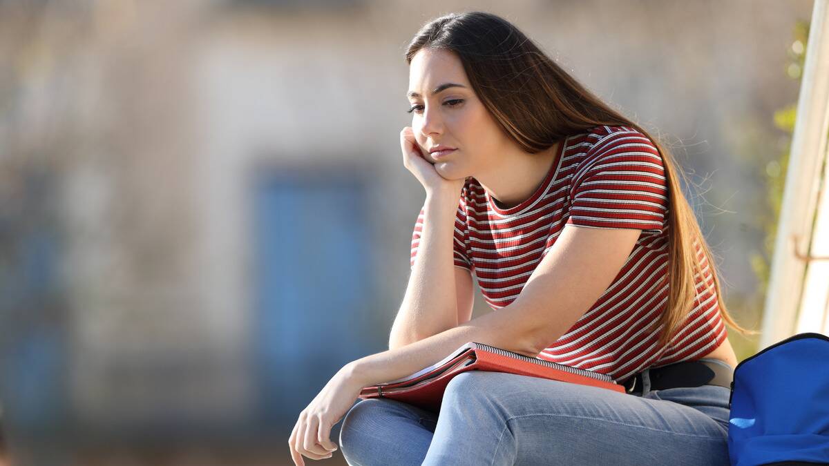 A woman sitting outside, her cheek in her hand, looking dejected and sad.