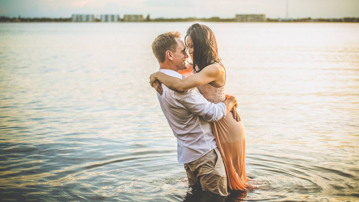 A couple standing in the water, holding onto each other, faces close, smiling.