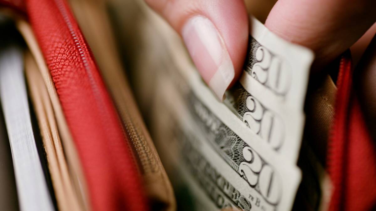 A closeup shot of someone pulling three fanned out $20 bills out of their wallet.