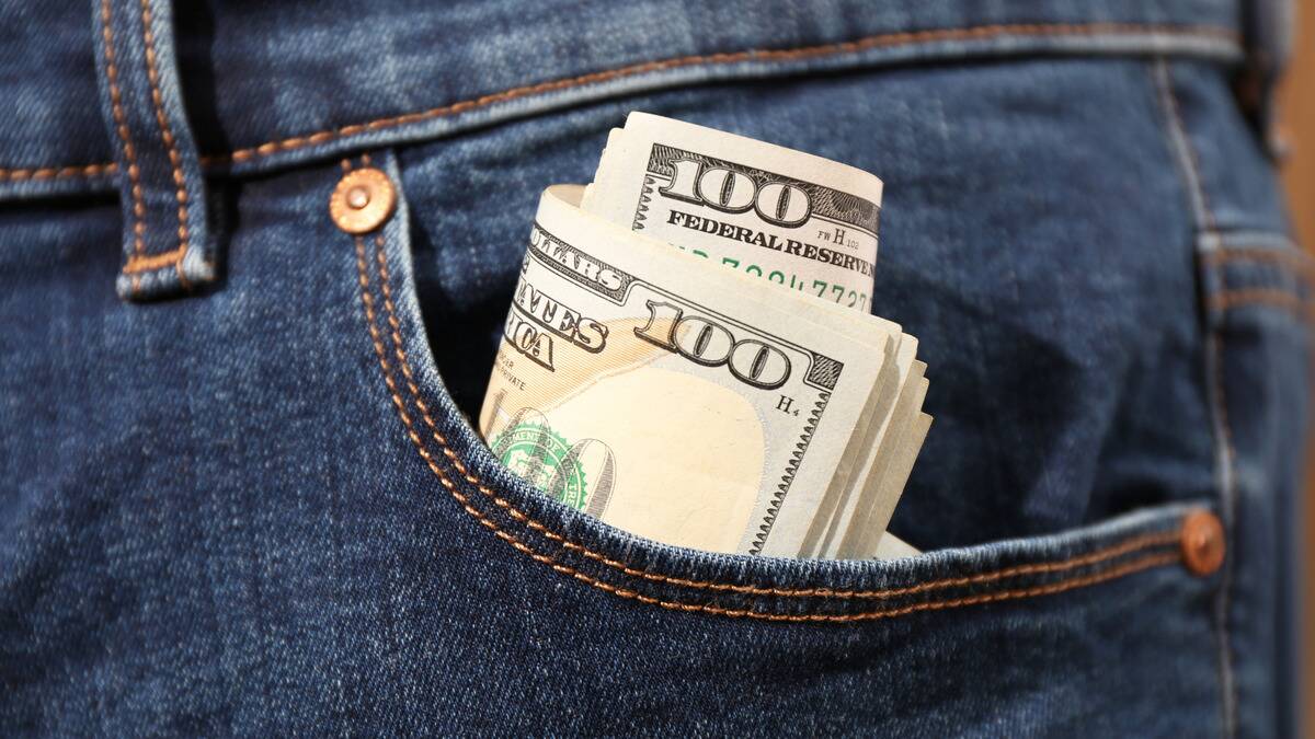 A close shot of a roll of $100 bills in someone's front denim pocket.