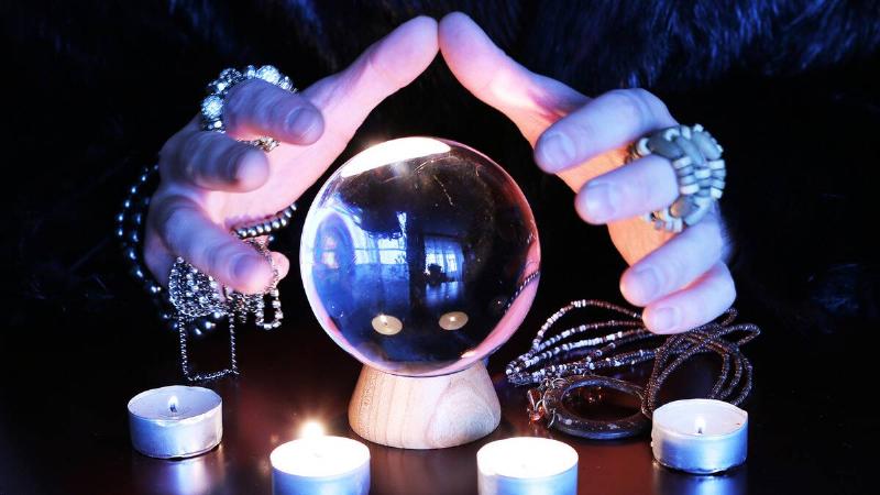 A woman's hands, adorned in a lot of jewelry, hovering around a crystal ball.