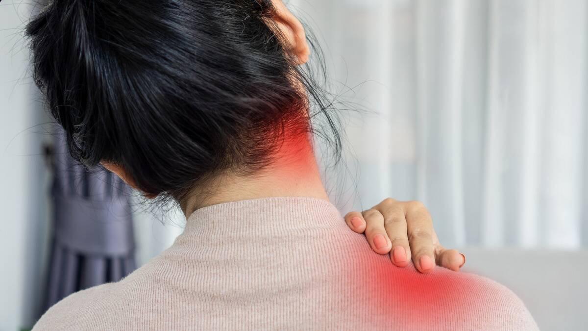 A close shot of a woman's neck and shoulder's from behind, two red glows displaying pain points, a hand massaging the point on her shoulder.