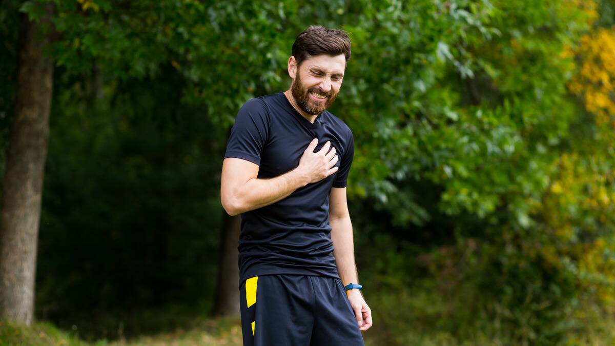 A man standing outside, presumably mid-run, clutching his chest in pain.