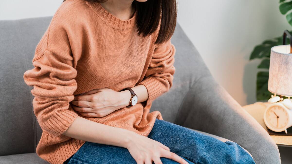 A close shot of a woman sitting on a couch, her arm clutching her stomach.