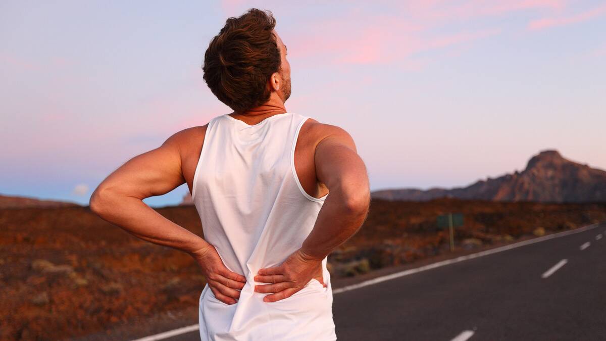 A man on the side of the road, presumably running, both hands on his lower back.