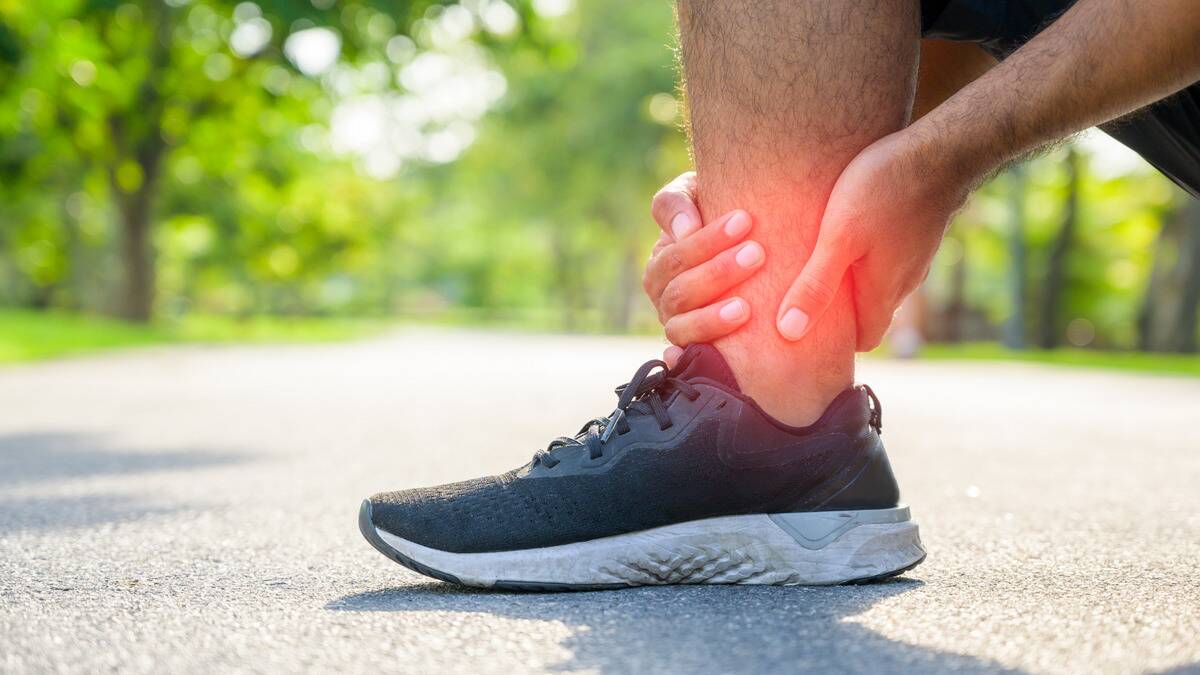 A close shot of a man's running shoe, hands massaging his ankle, a red glow emanating from it.