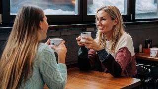 Two friends sitting on opposite sides of a cafe table, chatting over coffee.