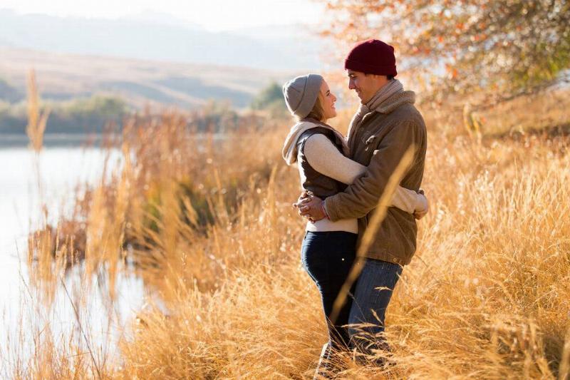A couple standing by a river among the reed grass, holding each other close.