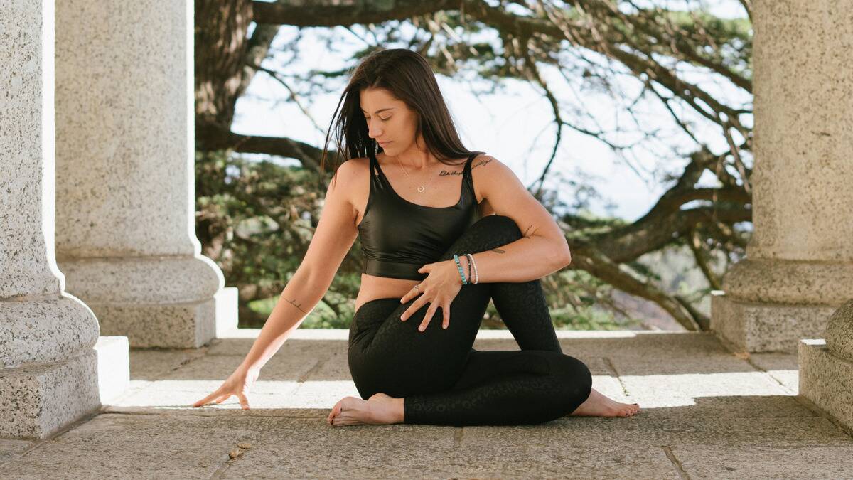 A woman sitting outside on a stone platform in a meditative yoga pattern.