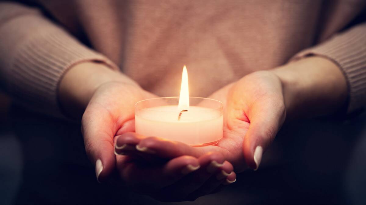 A close shot of someone with cupped hands holding a large tealight candle.