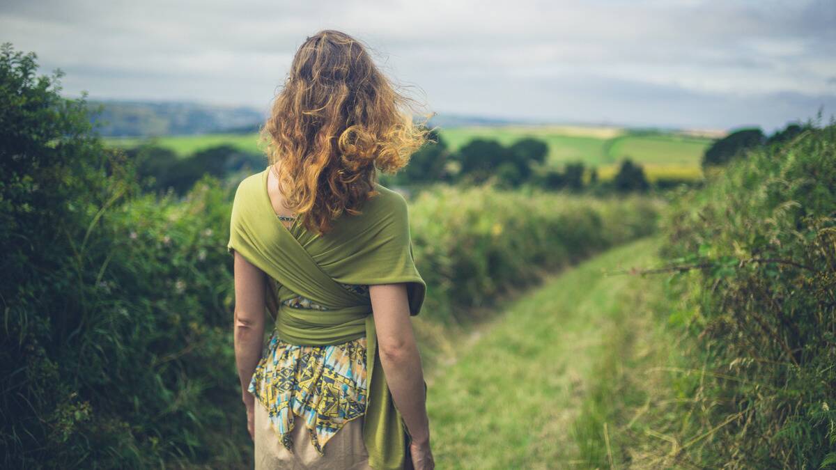 A woman facing away from the camera, walking out across a field.