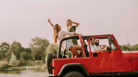 Four friends in a Jeep, two in the front and two standing up in the back, dancing.