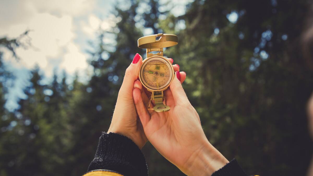 Someone holding up a compass in front of a blurred, tree-filled background.