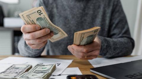 Someone holding a stack of $10 bills in one hand, using the other to count them.