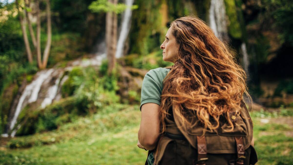 A woman shot from behind as she walks through a forest, looking off to the side.