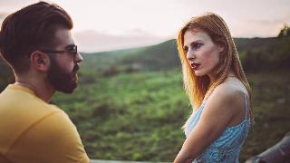 A couple standing outside, the woman looking at the man with a shocked expression, as if he'd just said something she disliked.