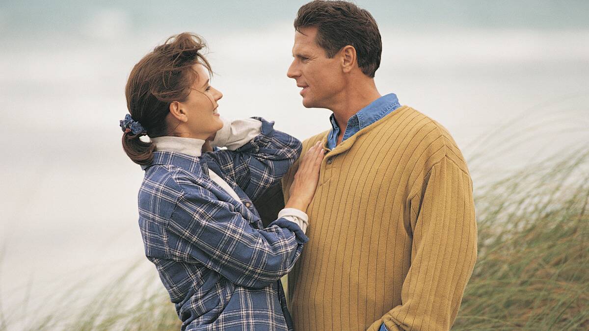 A couple standing outside in a windy field, the woman with her hand on the man's chest.