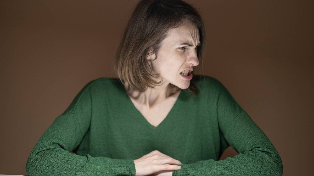 A woman with her arms folded on a table looking very angry, head turned to the side.