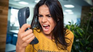 A close shot of a woman yelling angrily into an office phone.