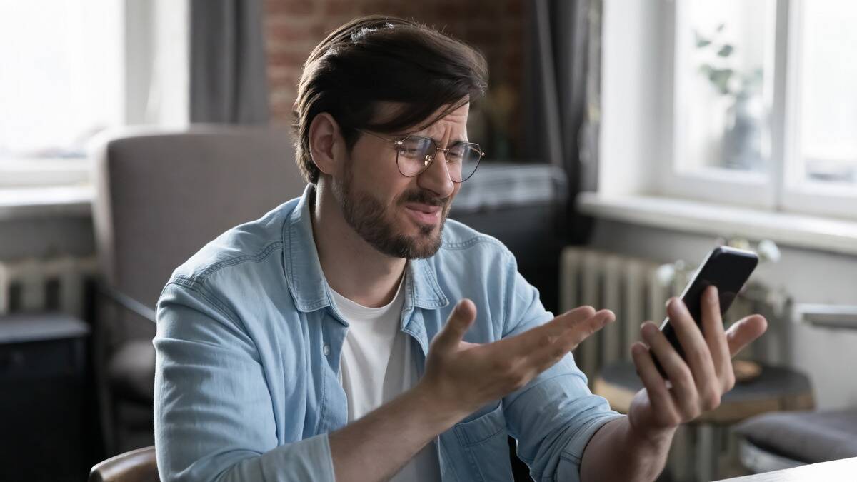 A man looking annoyed while gesturing at his phone.