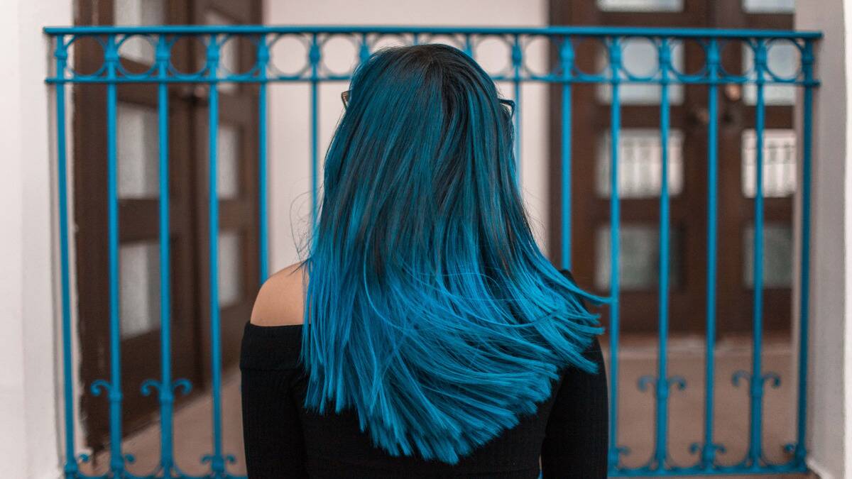 A bust shot of someone facing away from the camera, swishing their dyed blue hair just slightly.