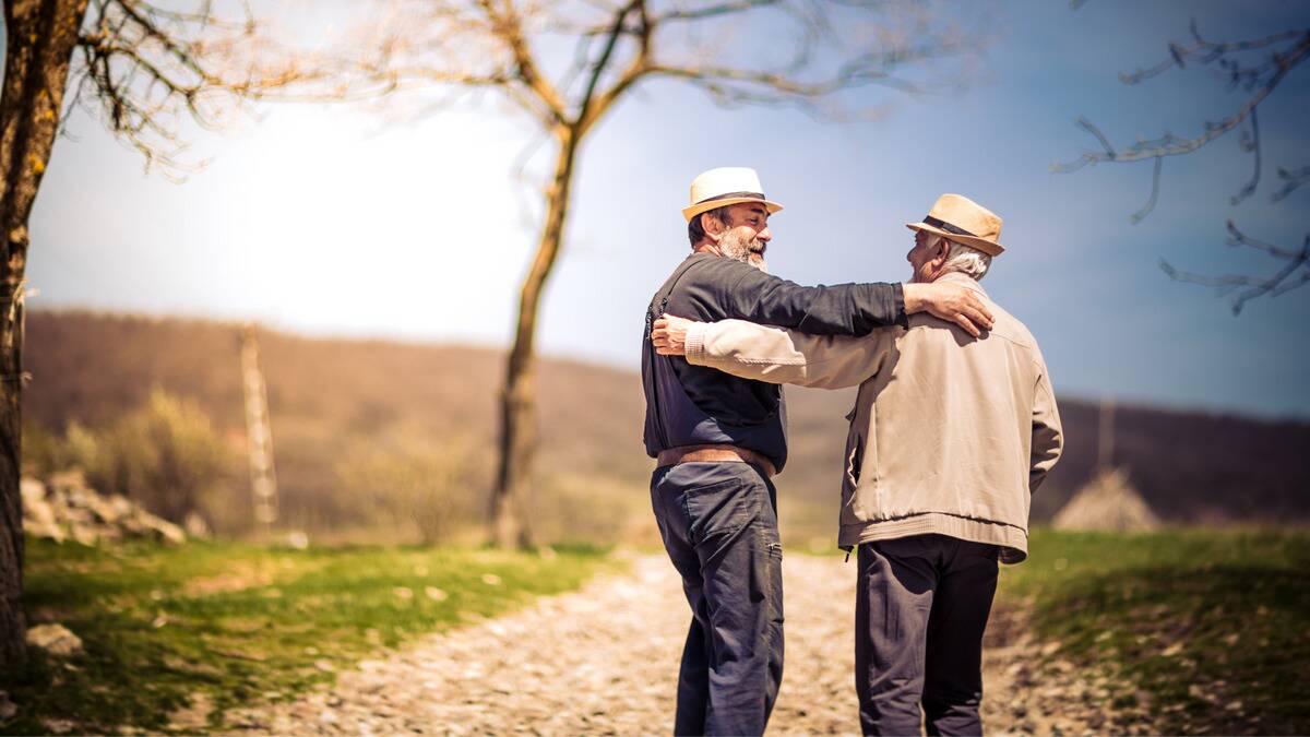 Two old friends reach out to embrace one another outside.